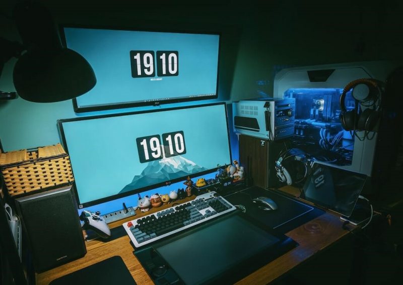 A gaming PC setup featuring a powerful computer tower with RGB lighting, a widescreen monitor displaying intense gameplay, a mechanical keyboard, and a gaming mouse.
